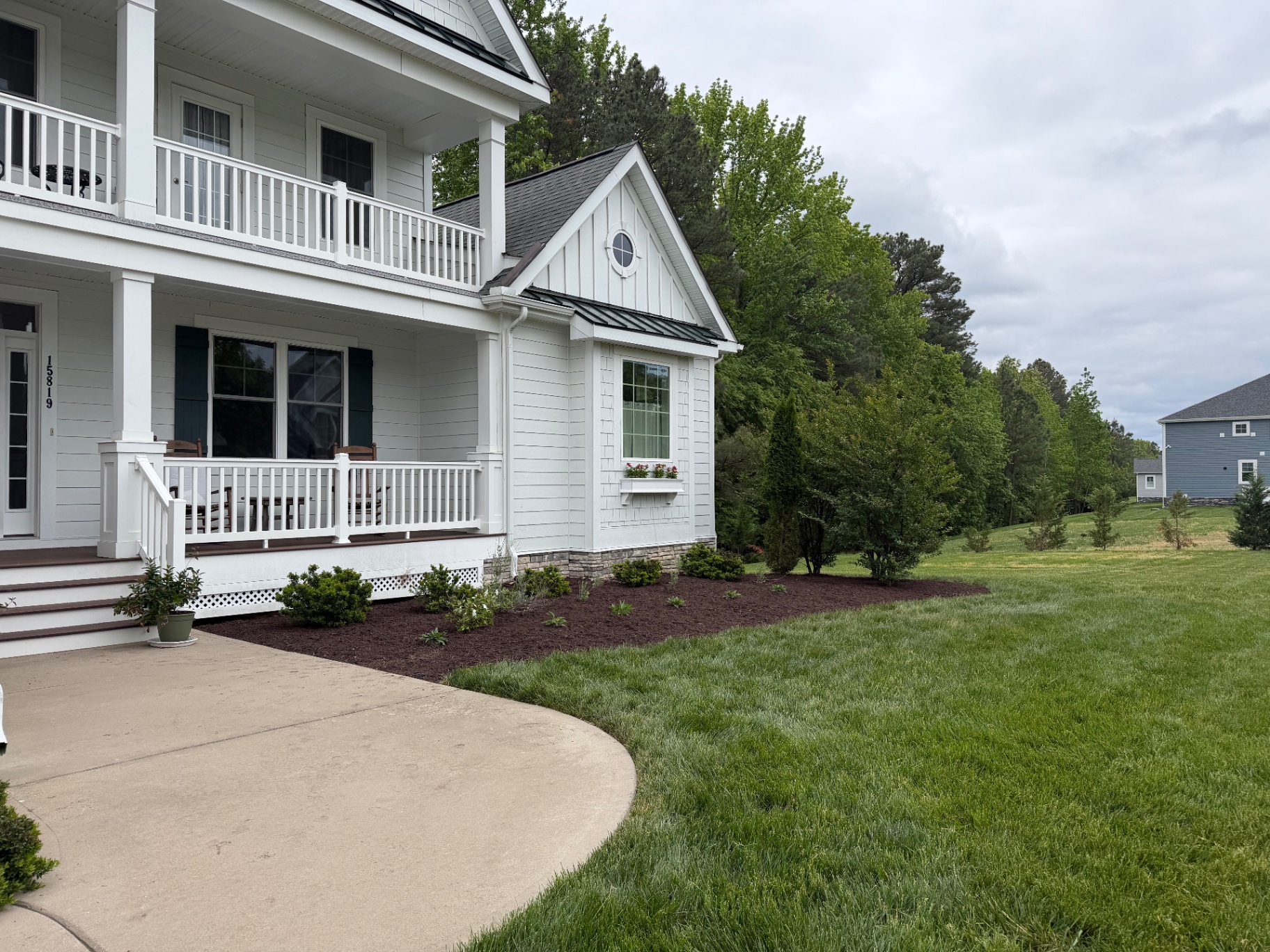 Front porch of a white farmhouse with freshly mulched foundation beds and a manicured lawn